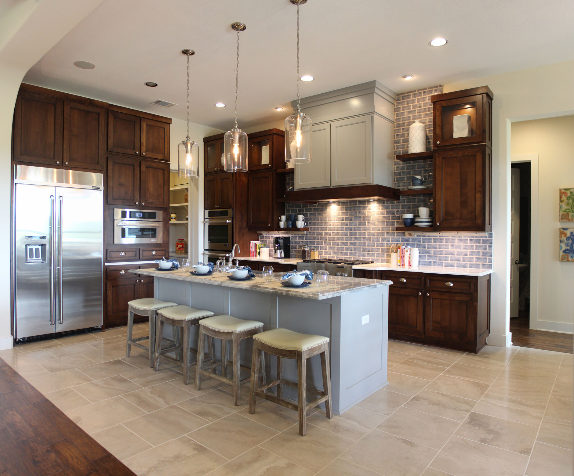 Burrows Cabinets' kitchen cabinet with Craftsman range hood at Travisso with stained cabinets, grey painted island and Terrazzo doors