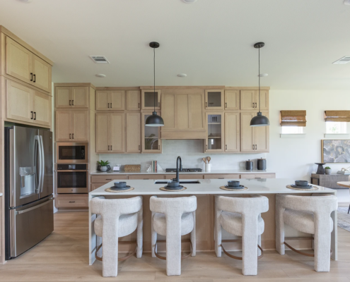 Kitchen cabinets in Maple Savaii with Shaker doors, tall uppers, glass doors, Shaker wood range hood and paneled island back