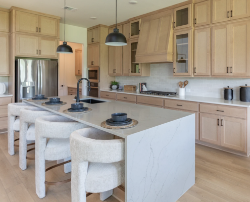 Kitchen in maple Savaii with Shaker doors with black pull handles and custom Shaker wood range hood, refrigerator shroud and waterfall island